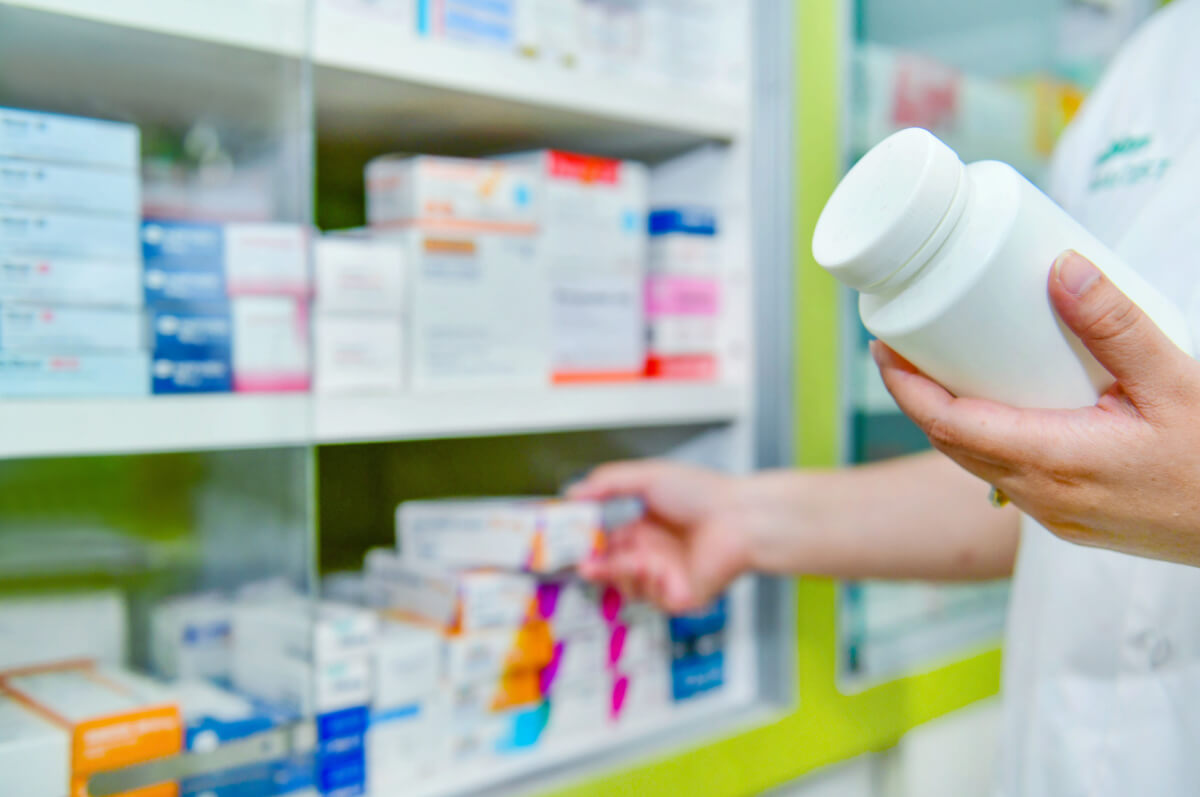 Pharmacist holding bottle of medicine and medicine box in pharmacy drugstore