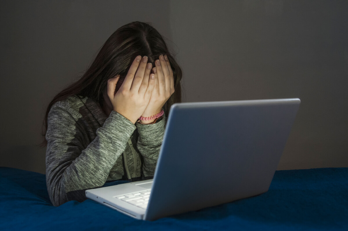 teenager with face in hands behind laptop