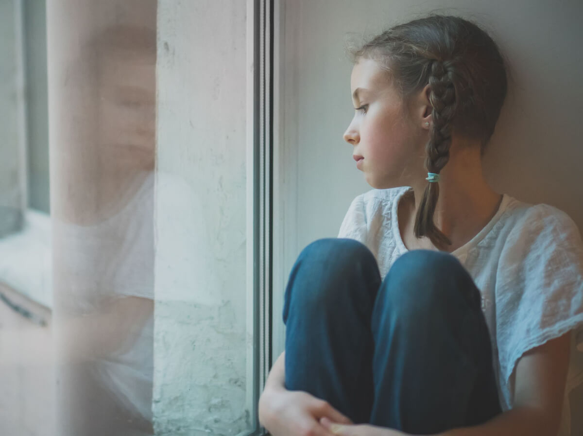 sad little girl sitting near window