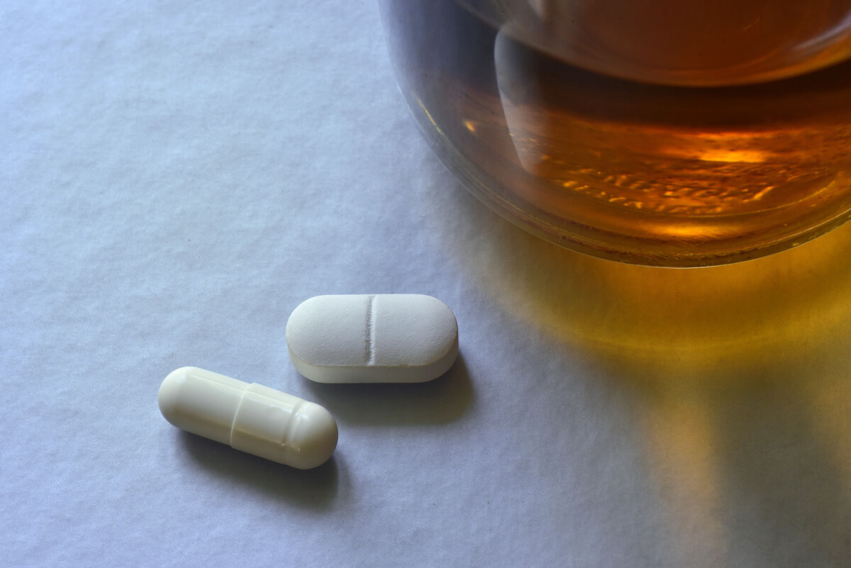 white pills near glass alcohol