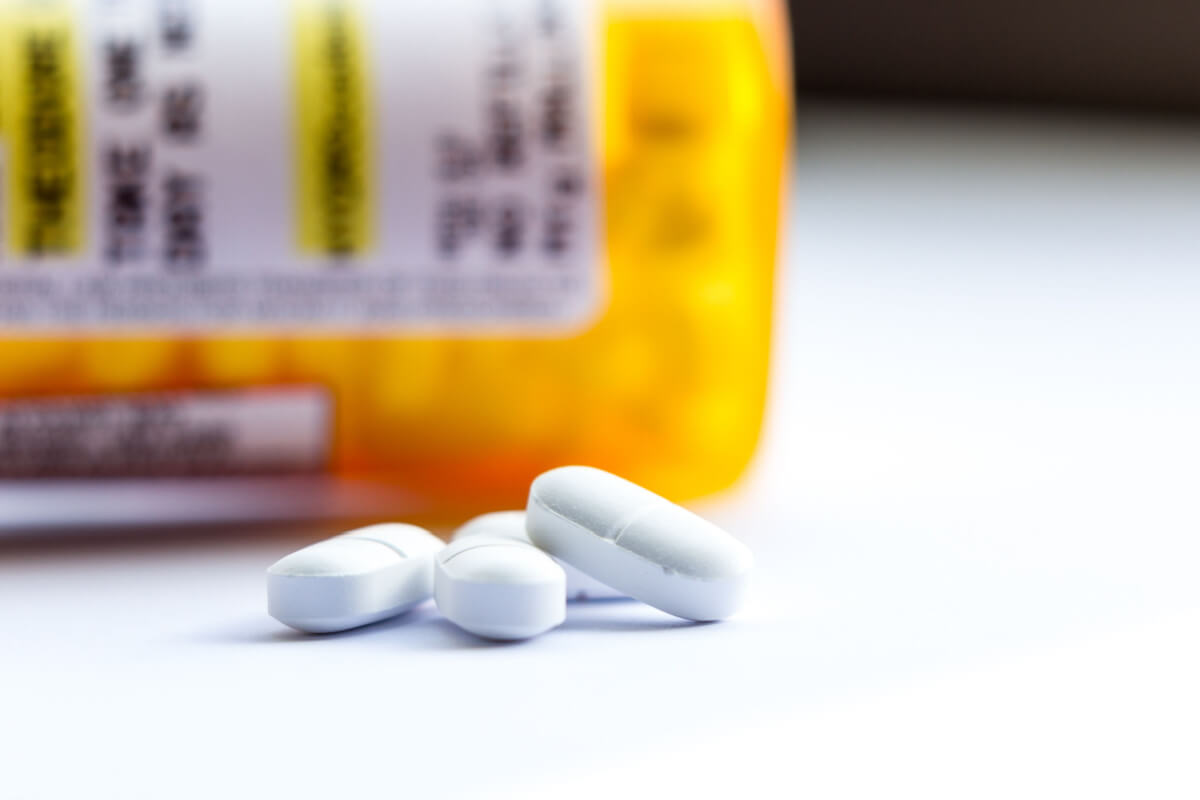 Close-up of a group of white tablets with an out of focus prescription bottle in the background