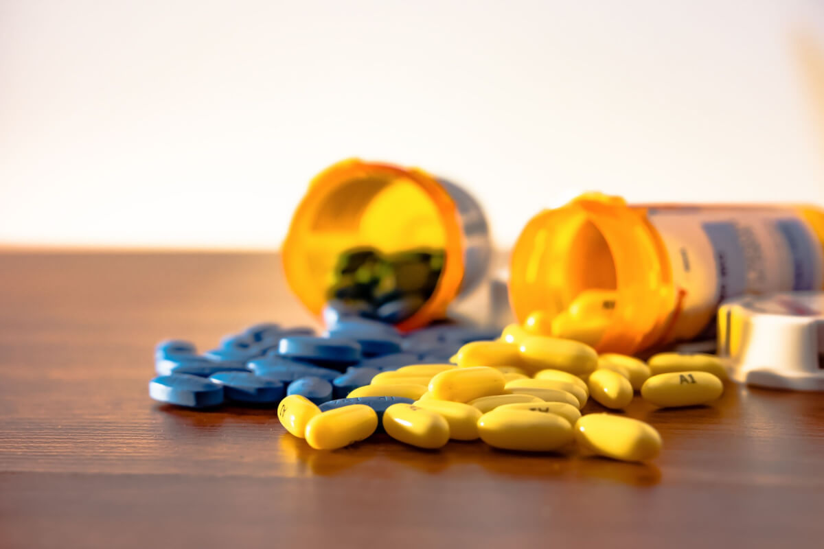Two prescription bottles overturned with blue and yellow pills spilling onto the wooden table
